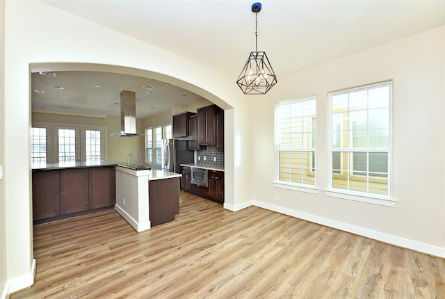 kitchen with dark brown cabinetry, stainless steel appliances, island range hood, sink, and kitchen peninsula