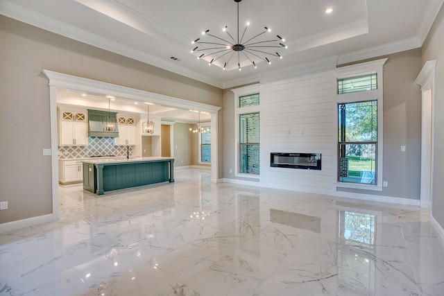 unfurnished living room with a large fireplace, crown molding, a chandelier, and a raised ceiling