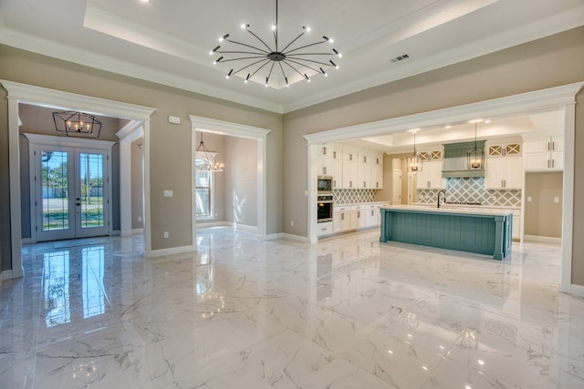 interior space featuring a center island with sink, a chandelier, white cabinetry, a tray ceiling, and hanging light fixtures