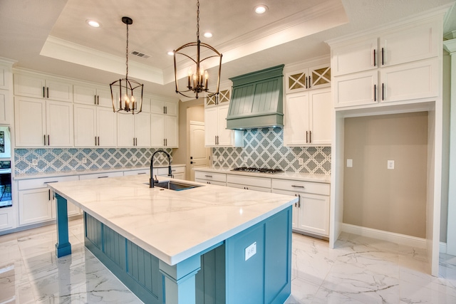 kitchen featuring a kitchen island with sink, hanging light fixtures, a tray ceiling, sink, and custom range hood