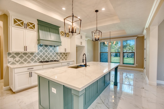 kitchen featuring sink, white cabinetry, decorative light fixtures, a raised ceiling, and a kitchen island with sink