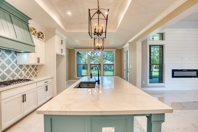 kitchen with a tray ceiling, decorative light fixtures, and a kitchen island with sink