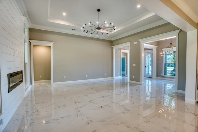 unfurnished living room with heating unit, a tray ceiling, ornamental molding, a large fireplace, and a chandelier