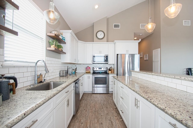 kitchen with appliances with stainless steel finishes, sink, white cabinetry, decorative light fixtures, and light stone countertops