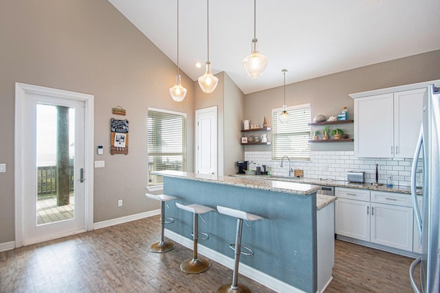 kitchen featuring light stone counters, white cabinetry, dark hardwood / wood-style floors, stainless steel fridge, and hanging light fixtures