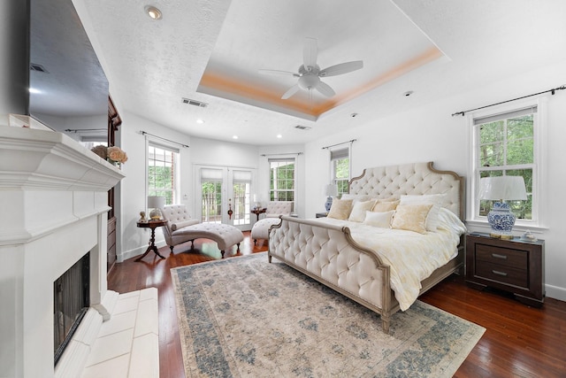 bedroom with a fireplace with raised hearth, hardwood / wood-style flooring, a raised ceiling, and visible vents