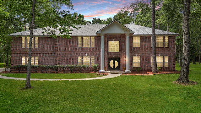 greek revival house with a standing seam roof, brick siding, metal roof, and a front lawn