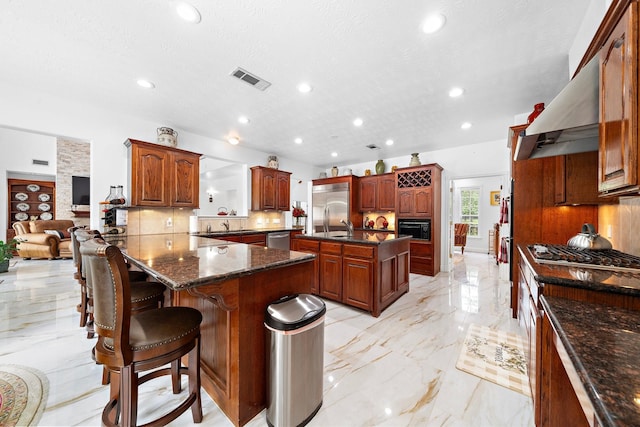 kitchen with a breakfast bar area, extractor fan, stainless steel appliances, marble finish floor, and backsplash