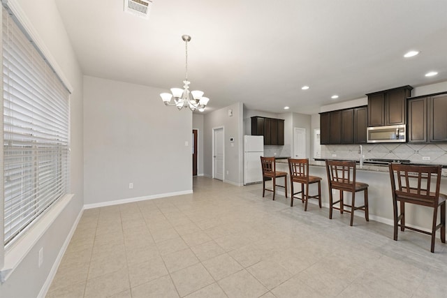 kitchen with white fridge, hanging light fixtures, dark brown cabinets, a breakfast bar area, and decorative backsplash