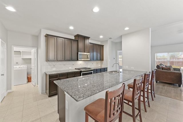 kitchen featuring stone countertops, stainless steel appliances, dark brown cabinetry, washer / clothes dryer, and sink