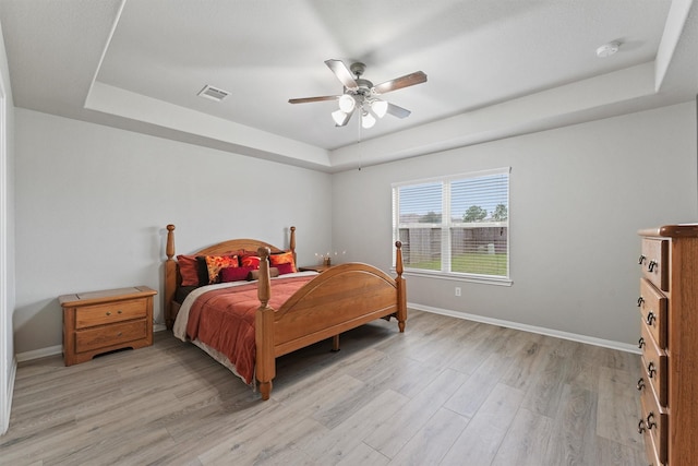 bedroom with light wood-type flooring, a tray ceiling, and ceiling fan