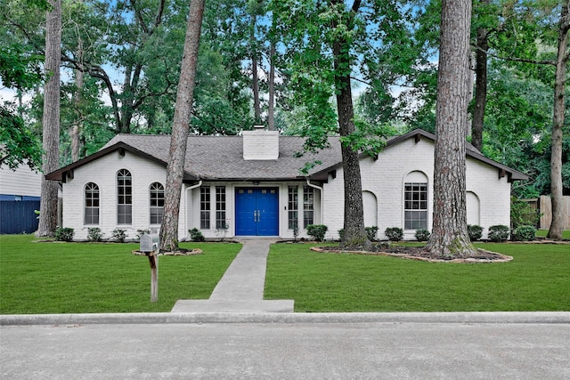 view of front of home featuring brick siding, a shingled roof, a front lawn, concrete driveway, and a chimney