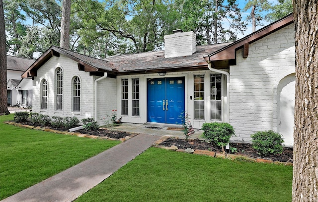 view of exterior entry with a lawn, brick siding, and a chimney