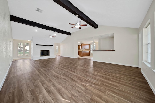 unfurnished living room with visible vents, a brick fireplace, vaulted ceiling with beams, and wood finished floors