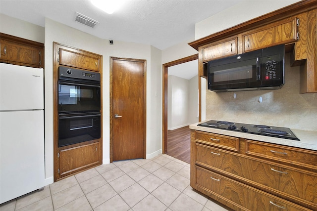 kitchen with light tile patterned floors, visible vents, black appliances, and brown cabinetry