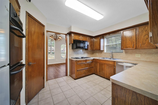 kitchen featuring light tile patterned floors, a healthy amount of sunlight, a sink, black appliances, and backsplash