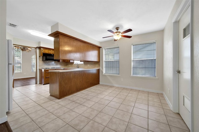 kitchen with visible vents, backsplash, a peninsula, brown cabinetry, and black microwave