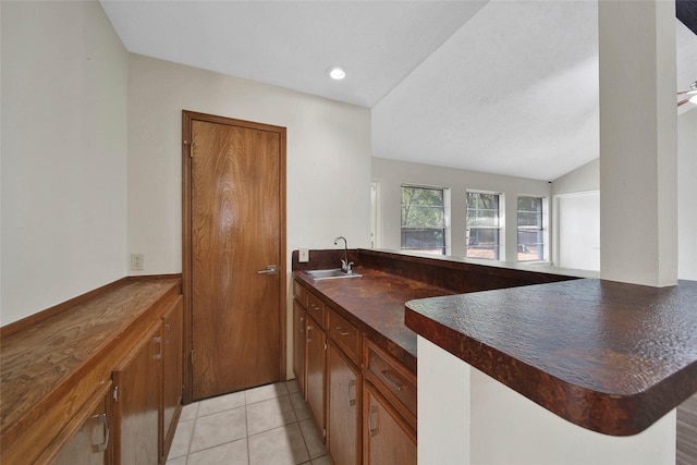 kitchen with a sink, dark countertops, a peninsula, light tile patterned floors, and vaulted ceiling