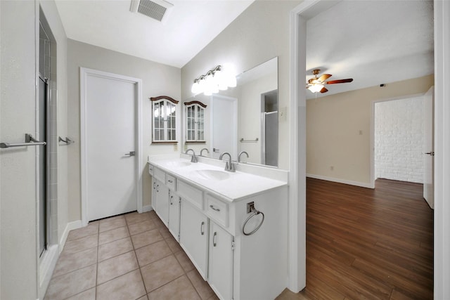 full bathroom with a shower with door, visible vents, double vanity, and a sink