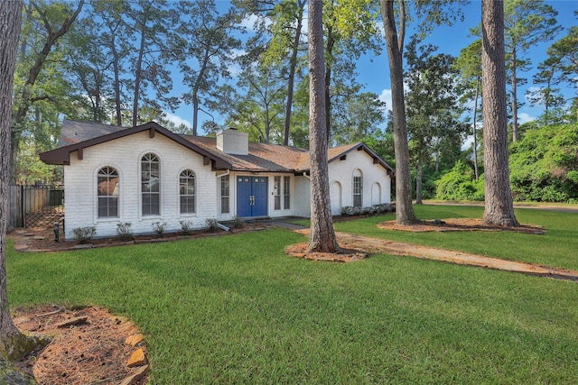 view of front of home featuring brick siding, a chimney, a front lawn, and fence