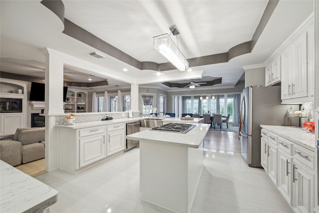 kitchen with kitchen peninsula, stainless steel appliances, light stone counters, a raised ceiling, and white cabinets