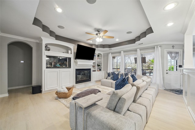 living room with light wood-type flooring, ceiling fan, built in shelves, and ornamental molding