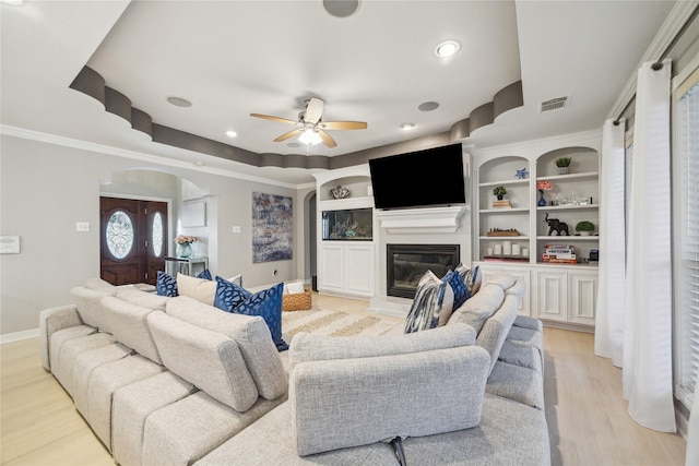 living room with light hardwood / wood-style floors, ceiling fan, a tray ceiling, and crown molding