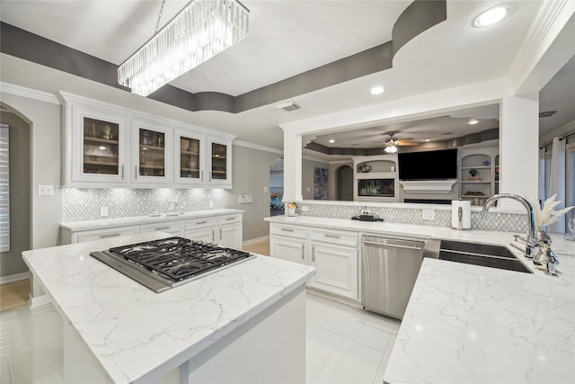 kitchen with kitchen peninsula, stainless steel appliances, sink, light stone counters, and white cabinets