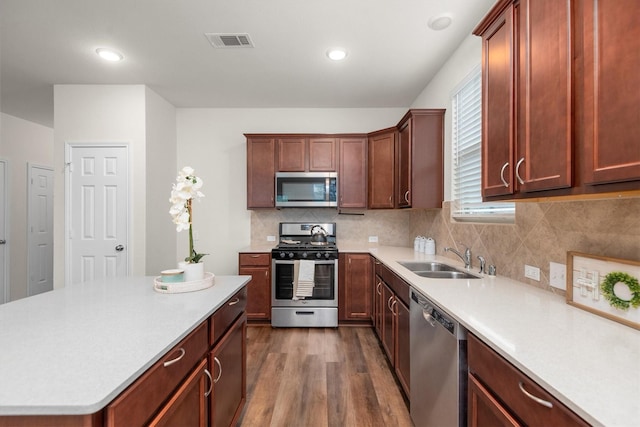 kitchen with appliances with stainless steel finishes, wood-type flooring, sink, a kitchen island, and tasteful backsplash