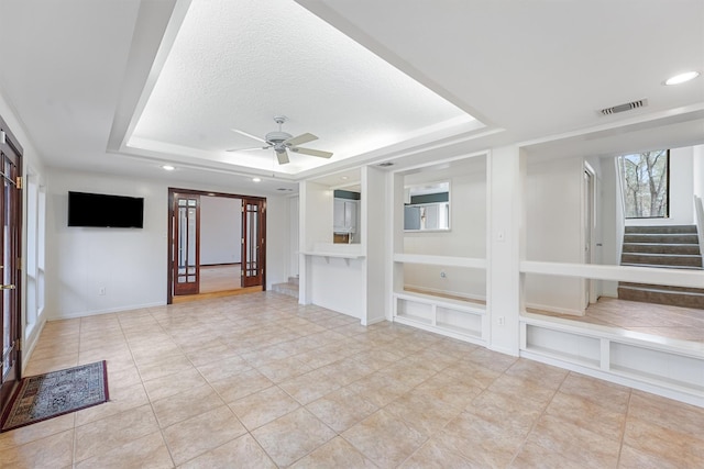 unfurnished living room featuring ceiling fan, stairway, a raised ceiling, and visible vents