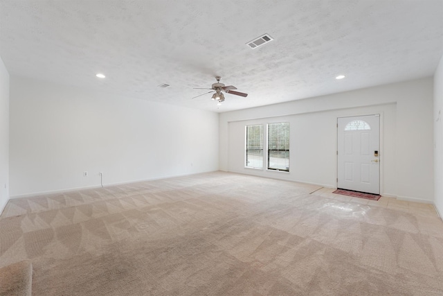 unfurnished living room with baseboards, visible vents, a textured ceiling, and light colored carpet