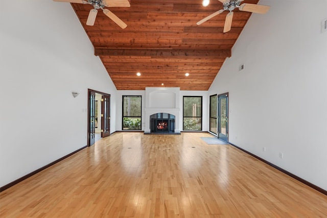 unfurnished living room with high vaulted ceiling, light wood-type flooring, a warm lit fireplace, and baseboards