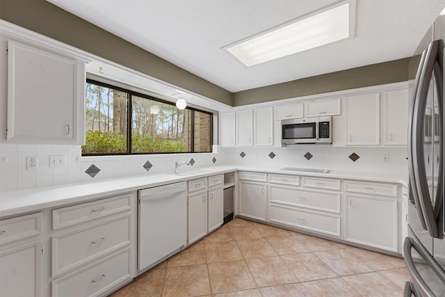 kitchen featuring light tile patterned floors, tasteful backsplash, stainless steel appliances, white cabinetry, and a sink