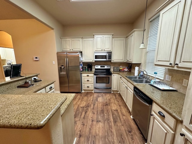 kitchen with hardwood / wood-style floors, sink, light stone counters, pendant lighting, and stainless steel appliances