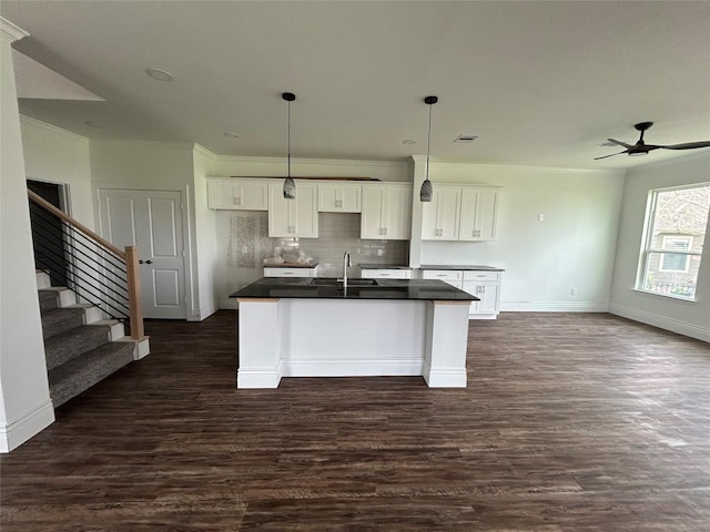 kitchen featuring a center island with sink, dark countertops, dark wood-style floors, white cabinetry, and a sink