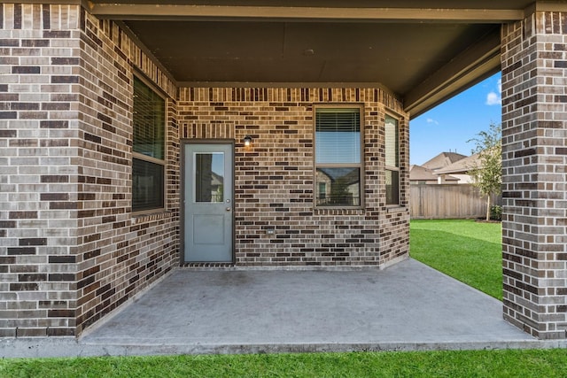 entrance to property featuring a patio area, fence, and brick siding