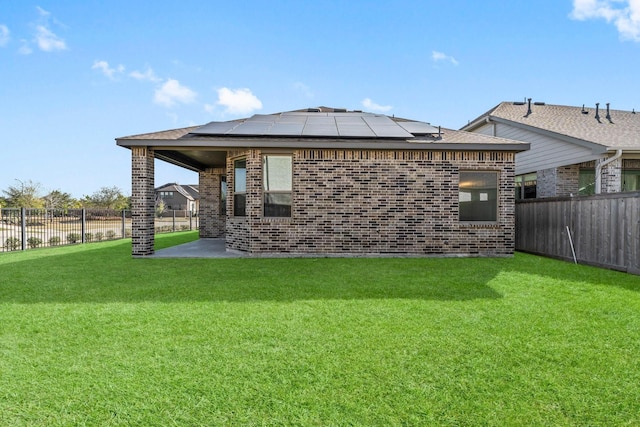 back of house featuring a yard, brick siding, solar panels, and a fenced backyard