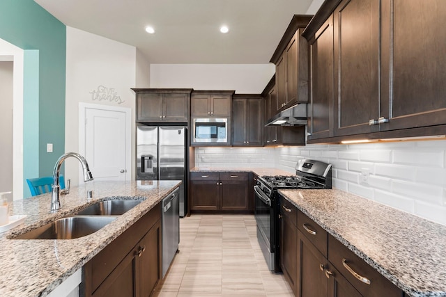 kitchen featuring light stone counters, stainless steel appliances, tasteful backsplash, a sink, and under cabinet range hood