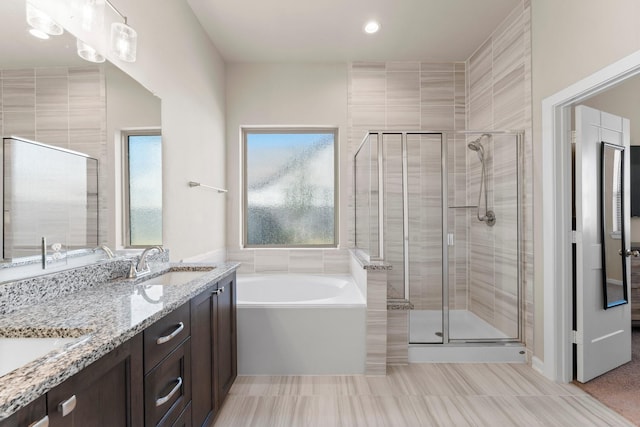 bathroom featuring a bath, a shower stall, double vanity, and a sink