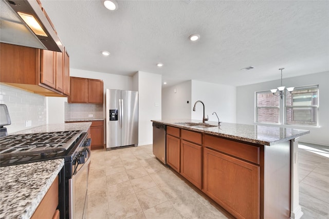 kitchen featuring stainless steel appliances, a sink, exhaust hood, brown cabinetry, and an island with sink