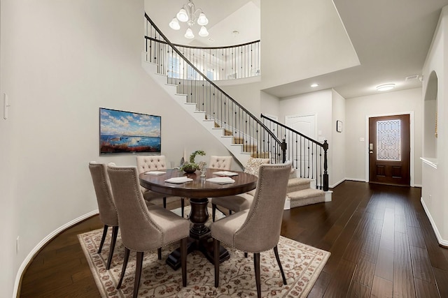 dining area with a notable chandelier, dark wood finished floors, a towering ceiling, stairway, and baseboards