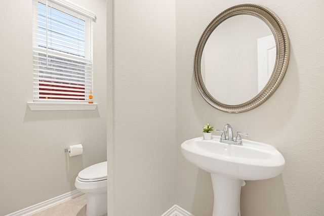 half bath featuring a sink, tile patterned flooring, toilet, and baseboards