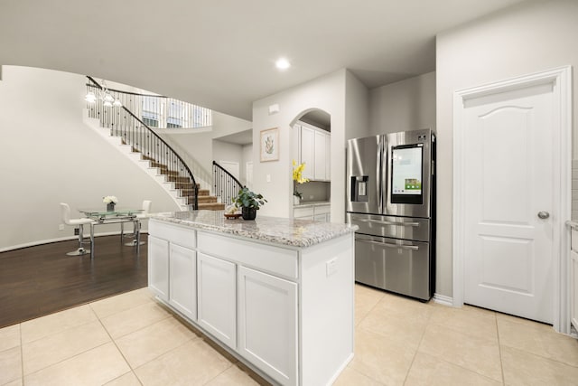 kitchen featuring light stone counters, a center island, stainless steel refrigerator with ice dispenser, light tile patterned floors, and white cabinets