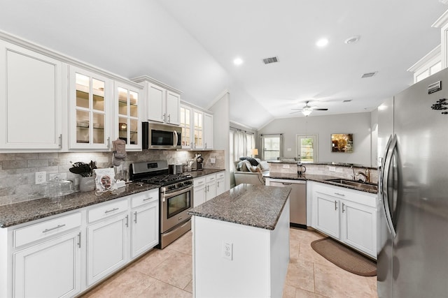 kitchen with stainless steel appliances, a sink, white cabinetry, a center island, and glass insert cabinets