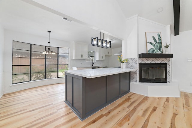 kitchen with white cabinetry, kitchen peninsula, a fireplace, an inviting chandelier, and light hardwood / wood-style floors