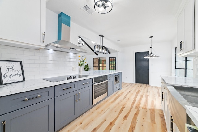 kitchen featuring white cabinetry, stainless steel appliances, wall chimney exhaust hood, and decorative light fixtures