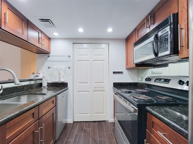 kitchen with stainless steel appliances, a sink, visible vents, wood tiled floor, and dark stone countertops