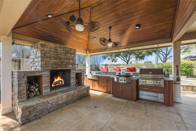 view of patio with exterior kitchen, an outdoor stone fireplace, area for grilling, sink, and a gazebo