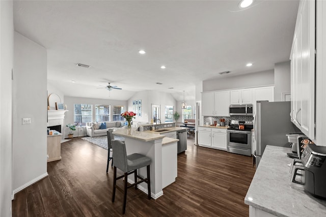 kitchen with an island with sink, stainless steel appliances, light stone countertops, white cabinets, and a kitchen breakfast bar