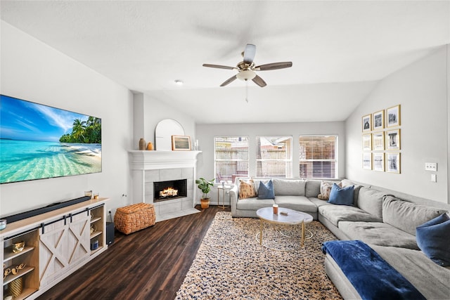 living room with dark hardwood / wood-style flooring, ceiling fan, a tiled fireplace, and lofted ceiling